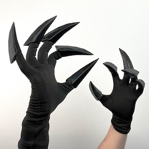 May include: A pair of black gloves with long, pointed, black claws attached to the fingertips. The gloves are made of a dark fabric, and the claws have a glossy finish. The claws are angled and pointed. Likely part of a costume or cosplay.
