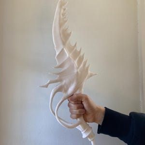 May include: A white 3D printed sword with a curved blade and a detailed, intricate design. The blade is sharp and pointed, and the handle is curved and has a textured surface.