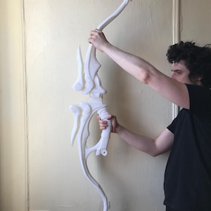 May include: A white 3D printed bow with a complex, intricate design. The bow is held by a person's hands.