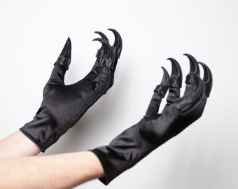 May include: A pair of black satin gloves with long, curved, claw-like tips. The gloves are displayed against a white background, showcasing the dramatic, gothic design. The gloves are a costume accessory.