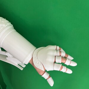 May include: White plastic 3D printed hand and forearm armor with segmented fingers and a decorative design on the forearm.