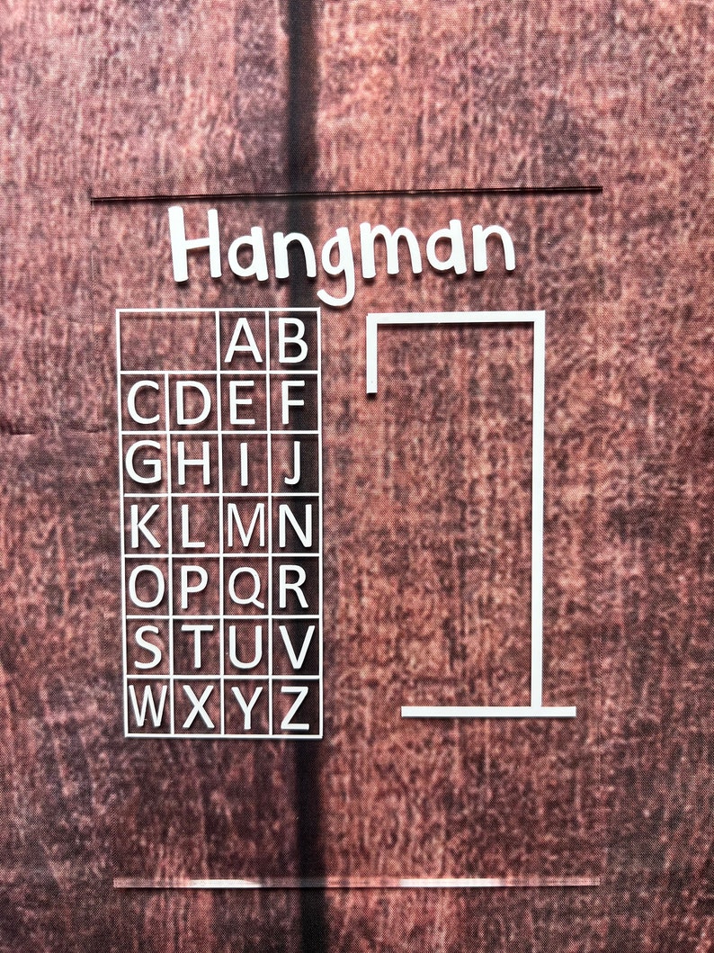 May include: A white Hangman game board with a grid of letters A through Z and a blank gallows. The board is on a brown textured background.
