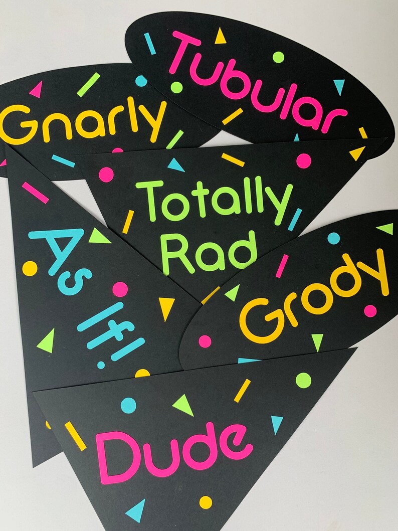 May include: A set of six black party decorations with neon pink, yellow, green, and blue accents. The decorations are shaped like triangles and ovals and feature the words "Gnarly", "Tubular", "Totally Rad", "As If", "Groovy", and "Dude".