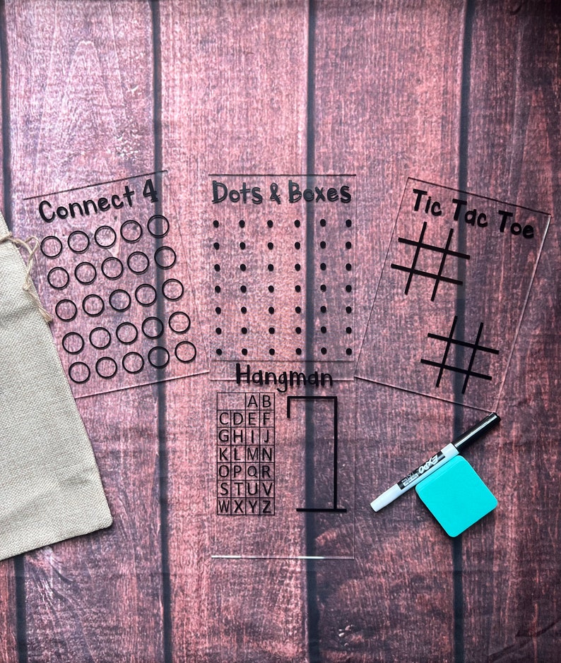 May include: Four clear acrylic game boards with black ink. The games are Connect 4, Dots & Boxes, Hangman, and Tic Tac Toe. The Hangman board includes the alphabet. A white dry-wipe marker and a blue sticky note are also included.