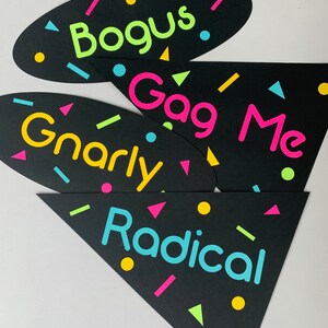 May include: Four black photo booth props with neon colored text and confetti. The props say "Bogus", "Gag Me", "Gnarly", and "Radical".