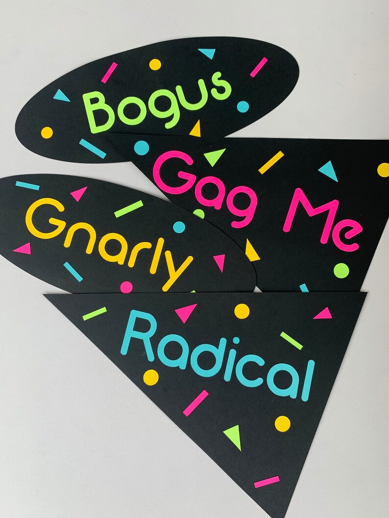 May include: Four black photo booth props with neon colored text and confetti. The props say "Bogus", "Gag Me", "Gnarly", and "Radical".