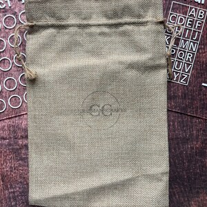 May include: A beige burlap drawstring bag with a brown drawstring. The bag is sitting on a wooden surface.