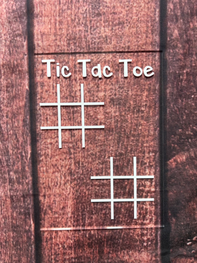 May include: A white sign with the words "Tic Tac Toe" written on it. The sign has two tic-tac-toe grids drawn on it.