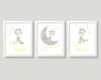 Op de afbeelding: Drie ingelijste prints met een schattige grijze giraffe met gele accenten op een witte wolk met zilveren glittersterren. De middelste print heeft een zilveren glitter halve maan.