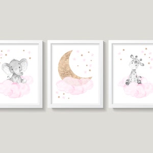 May include: Three framed prints with a watercolor style design. The first print features a gray elephant sitting on a pink cloud with gold stars. The second print features a gold crescent moon on a pink cloud with gold stars. The third print features a gray giraffe sitting on a pink cloud with gold stars.
