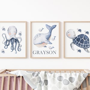 May include: Three watercolor prints featuring a blue octopus, a whale, and a turtle. The whale print has the name Grayson written below it.