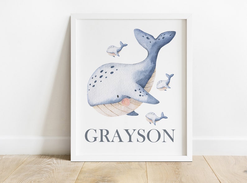 May include: A watercolor illustration of a blue whale with smaller whales swimming around it. The whale has a light blue body with dark blue spots and a light brown belly. The name "GRAYSON" is written in gray text below the whale.