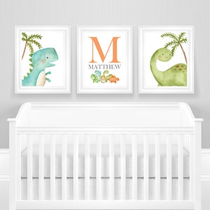 May include: Three framed prints with a dinosaur theme. The center print features the letter "M" in orange with the name "MATTHEW" below it. The left print shows a blue dinosaur with a palm tree. The right print shows a green dinosaur with a palm tree.