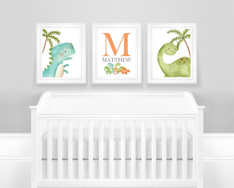 May include: Three framed prints with a dinosaur theme. The center print features the letter "M" in orange with the name "MATTHEW" below it. The left print shows a blue dinosaur with a palm tree. The right print shows a green dinosaur with a palm tree.