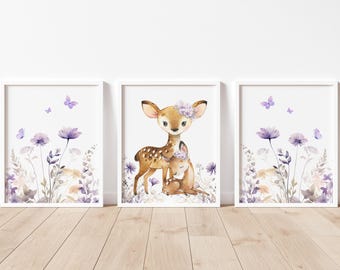 Op de afbeelding: Set van drie ingelijste aquarelprints. De middelste print toont een hertje met een bloemenkrans dat een ander hertje omhelst. De andere twee prints tonen paarse bloemen en vlinders. De frames zijn wit.