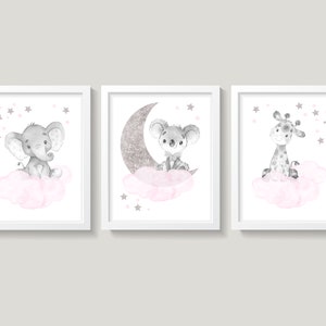 Op de afbeelding: Drie ingelijste prints met een witte achtergrond en een roze wolk met een grijs dier op elk. De eerste print toont een olifant, de tweede een koala op een zilveren glittermaan en de derde een giraffe. Elke print heeft roze sterren die rond het dier zijn verspreid.