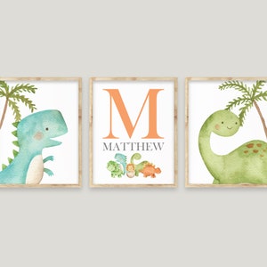 May include: Three framed prints featuring a green and blue dinosaur with a palm tree, the letter M in orange, and the name Matthew in grey, and a green dinosaur with a palm tree.