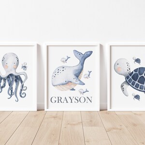 May include: Three watercolor prints featuring a blue octopus, a blue whale, and a blue sea turtle. The whale print has the name Grayson written below it.