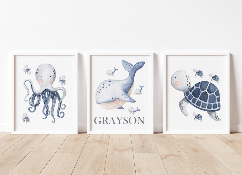 May include: Three watercolor prints featuring a blue octopus, a blue whale, and a blue sea turtle. The whale print has the name Grayson written below it.