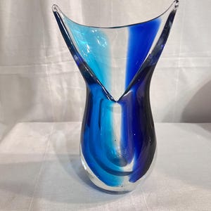 May include: A blue and turquoise glass vase with a unique, twisted design. The vase has a wide mouth and a narrow base.