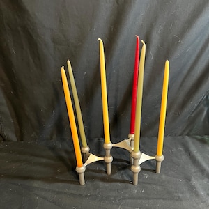 May include: A metal candle holder with six colorful taper candles. The candles are in shades of yellow, green, and red. The candle holder has a silver finish and a geometric design. Home decor.