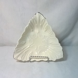May include: A white ceramic triangular serving dish with a silver rim and a decorative embossed design. The dish is on a metal stand.