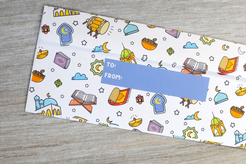 May include: A white envelope with a blue label that says "TO: FROM:". The envelope is decorated with a pattern of Islamic symbols, including stars, crescents, mosques, and prayer rugs.