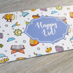 May include: A white card with a blue and white banner that says "Happy Eid!" The card is decorated with a pattern of colorful Islamic symbols, including crescent moons, stars, mosques, and lanterns.