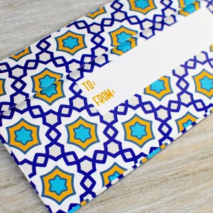 May include: A white gift tag with a blue and yellow geometric pattern. The tag has the words "TO:" and "FROM:" printed on it.