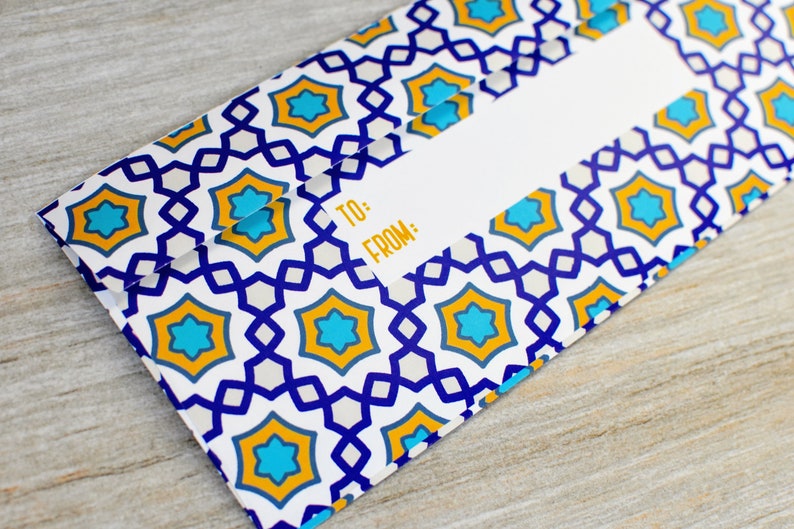May include: A white gift tag with a blue and yellow geometric pattern. The tag has the words "TO:" and "FROM:" printed on it.