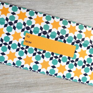 May include: A white envelope with a geometric pattern of teal, black, and yellow stars. The envelope has a yellow label with the words "TO:" and "FROM:" printed on it.