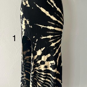 K&ouml;nnte beinhalten: Ein schwarzer und cremefarbener Maxirock mit Batikmuster. Der Rock hat eine hohe Taille und einen Seitenschlitz. Der Stoff hat ein wirbelndes Muster aus Schwarz und Creme, das einen einzigartigen Look erzeugt. Der Rock wird auf einer Schaufensterpuppe pr&auml;sentiert.