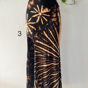 K&ouml;nnte beinhalten: Ein schwarz-beiger Batikrock mit hoher Taille und Seitenschlitz. Der Rock hat ein Sonnenmuster und die Zahl "3" ist auf der Vorderseite sichtbar. Der Rock wird auf einer Schaufensterpuppe pr&auml;sentiert.