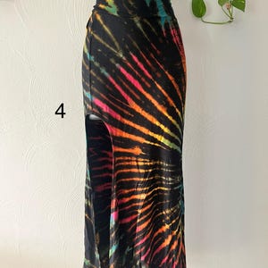 K&ouml;nnte beinhalten: Langer, schwarzer Batikrock mit hohem Bund und Seitenschlitz. Der Rock hat leuchtende Streifen in Pink, Orange, Gelb und T&uuml;rkis. Die Zahl "4" ist auf der linken Seite des Rocks zu sehen.