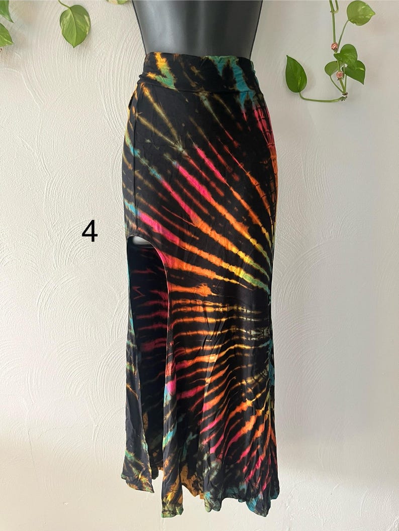 K&ouml;nnte beinhalten: Langer, schwarzer Batikrock mit hohem Bund und Seitenschlitz. Der Rock hat leuchtende Streifen in Pink, Orange, Gelb und T&uuml;rkis. Die Zahl "4" ist auf der linken Seite des Rocks zu sehen.