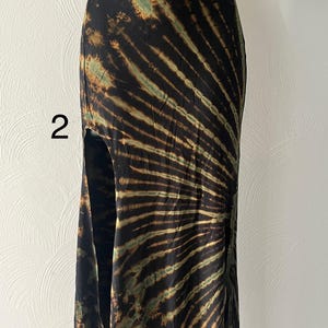 K&ouml;nnte beinhalten: Schwarzer Maxirock mit Batikmuster in Braun- und Gr&uuml;nt&ouml;nen. Der Rock hat einen hohen Schlitz auf der linken Seite. Der Stoff wirkt weich und flie&szlig;end, geeignet f&uuml;r Freizeitkleidung. Der Rock wird auf einer Schaufensterpuppe pr&auml;sentiert.