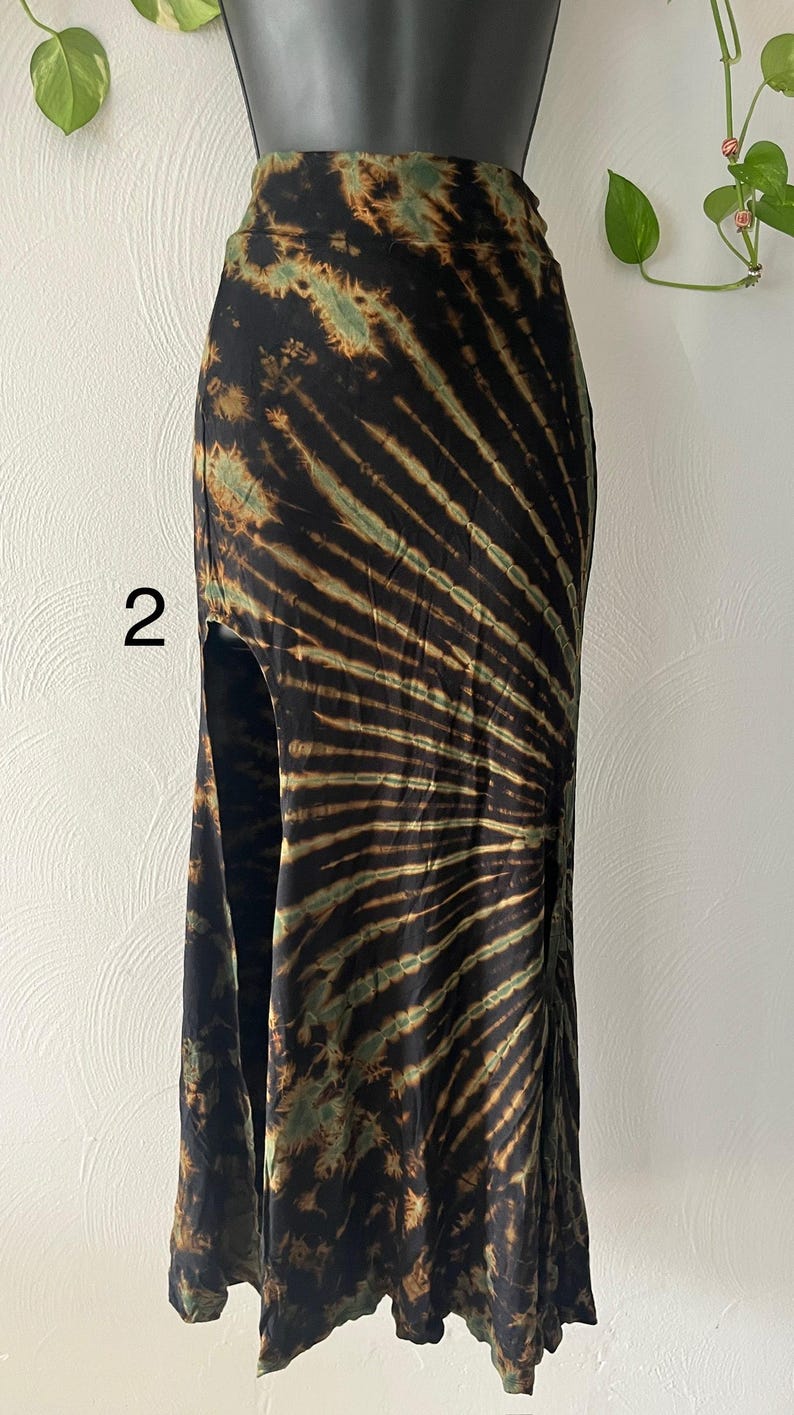 K&ouml;nnte beinhalten: Schwarzer Maxirock mit Batikmuster in Braun- und Gr&uuml;nt&ouml;nen. Der Rock hat einen hohen Schlitz auf der linken Seite. Der Stoff wirkt weich und flie&szlig;end, geeignet f&uuml;r Freizeitkleidung. Der Rock wird auf einer Schaufensterpuppe pr&auml;sentiert.