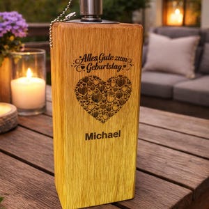 Puede incluir: Un portavelas rectangular de madera con tapa y cadena met&aacute;licas. La parte delantera presenta el texto "Alles Gute zum Geburtstag" sobre un coraz&oacute;n hecho de corazones m&aacute;s peque&ntilde;os, y el nombre "Michael" debajo. La madera tiene un degradado.