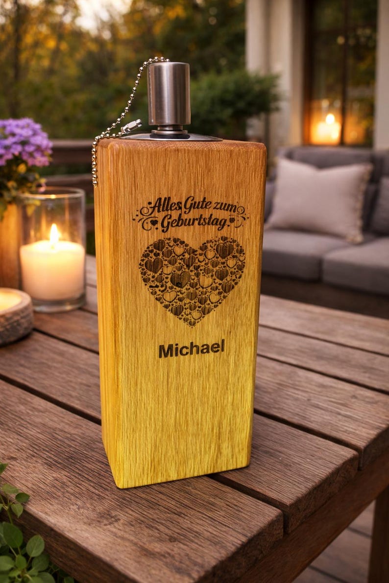 Puede incluir: Un portavelas rectangular de madera con tapa y cadena met&aacute;licas. La parte delantera presenta el texto "Alles Gute zum Geburtstag" sobre un coraz&oacute;n hecho de corazones m&aacute;s peque&ntilde;os, y el nombre "Michael" debajo. La madera tiene un degradado.
