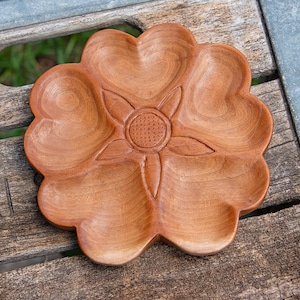 May include: A wooden serving dish shaped like a flower with five petals. The dish is made of light brown wood and has a carved sunflower design in the center.