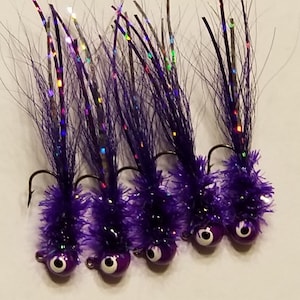 May include: Five purple and silver fishing lures with a fuzzy texture and a black hook. The lures have a round, black eye and a silver hook.
