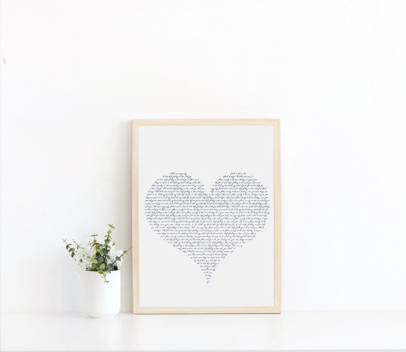 May include: A framed print of a heart-shaped design made of handwritten text in navy blue ink on a white background. The frame is light wood.