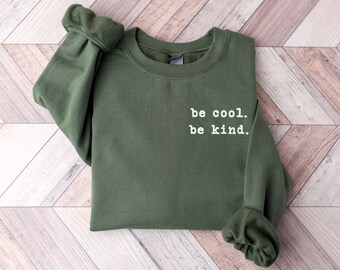 May include: A dark green sweatshirt with the text "be cool. be kind." printed in white on the front.