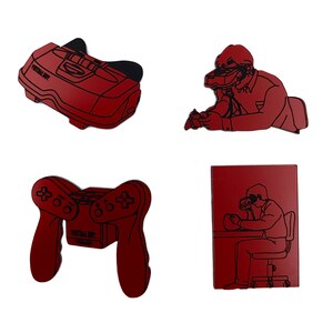May include: Four red and black laser-cut wooden pins featuring a virtual reality headset, a video game console, a video game controller, and a person wearing a virtual reality headset. The pins are all in the same style and have a retro look.