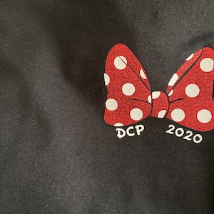 May include: Black t-shirt with a red bow with white polka dots. The bow has the text "DCP 2020" underneath.
