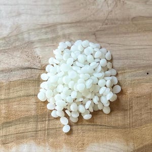 May include: A pile of white wax beads on a wooden surface.