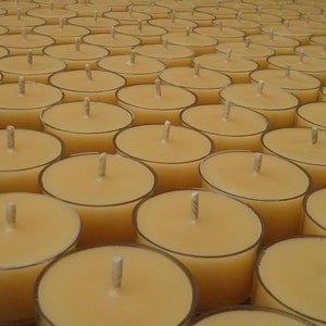 May include: A close-up view of a large quantity of small, round, yellow tea light candles arranged in a grid pattern. The candles are in clear plastic containers with a wick in the centre of each candle.