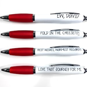 May include: Four white pens with red caps and different humorous messages printed on them. The messages are "EW, DAVID", "FOLD IN THE CHEESE", "BEST WISHES, WARMEST REGARDS", and "LOVE THAT JOURNEY FOR ME".
