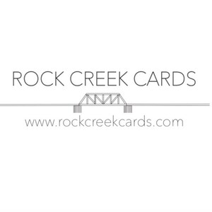 Puede incluir: Logotipo minimalista de Rock Creek Cards con el texto "ROCK CREEK CARDS" en una fuente limpia y sin serifa. Debajo, un gr&aacute;fico de puente estilizado y la direcci&oacute;n web www.rockcreekcards.com.