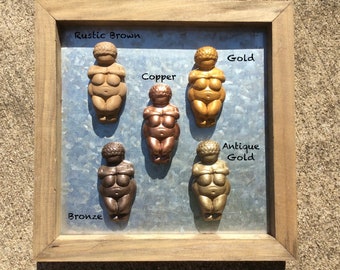 Pode incluir: Uma moldura com seis pequenas estatuetas de cerâmica, cada uma representando uma figura feminina em um acabamento metálico diferente: marrom rústico, dourado, cobre, dourado antigo e bronze. A moldura tem um acabamento de madeira rústica.